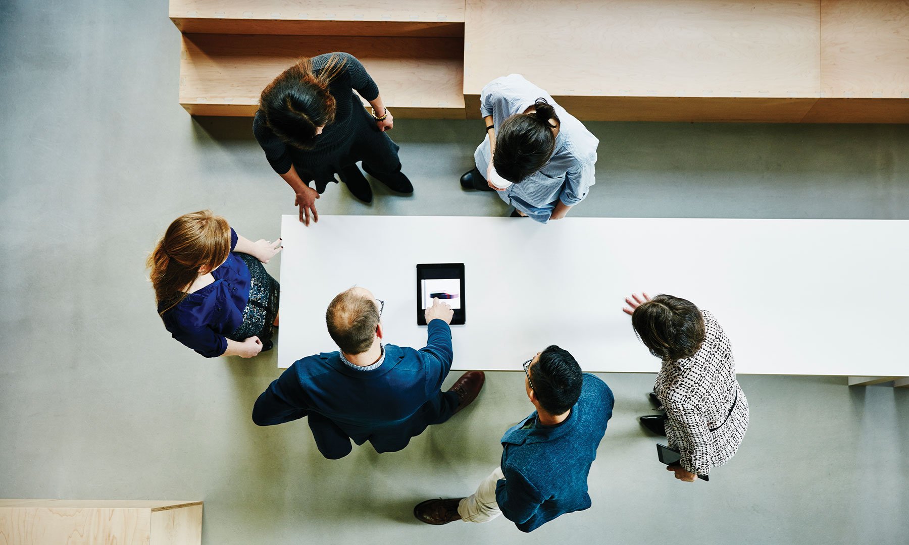 Directly above shot of diverse group of business people having a project meeting, using digital tablet, brainstorming and strategizing together.